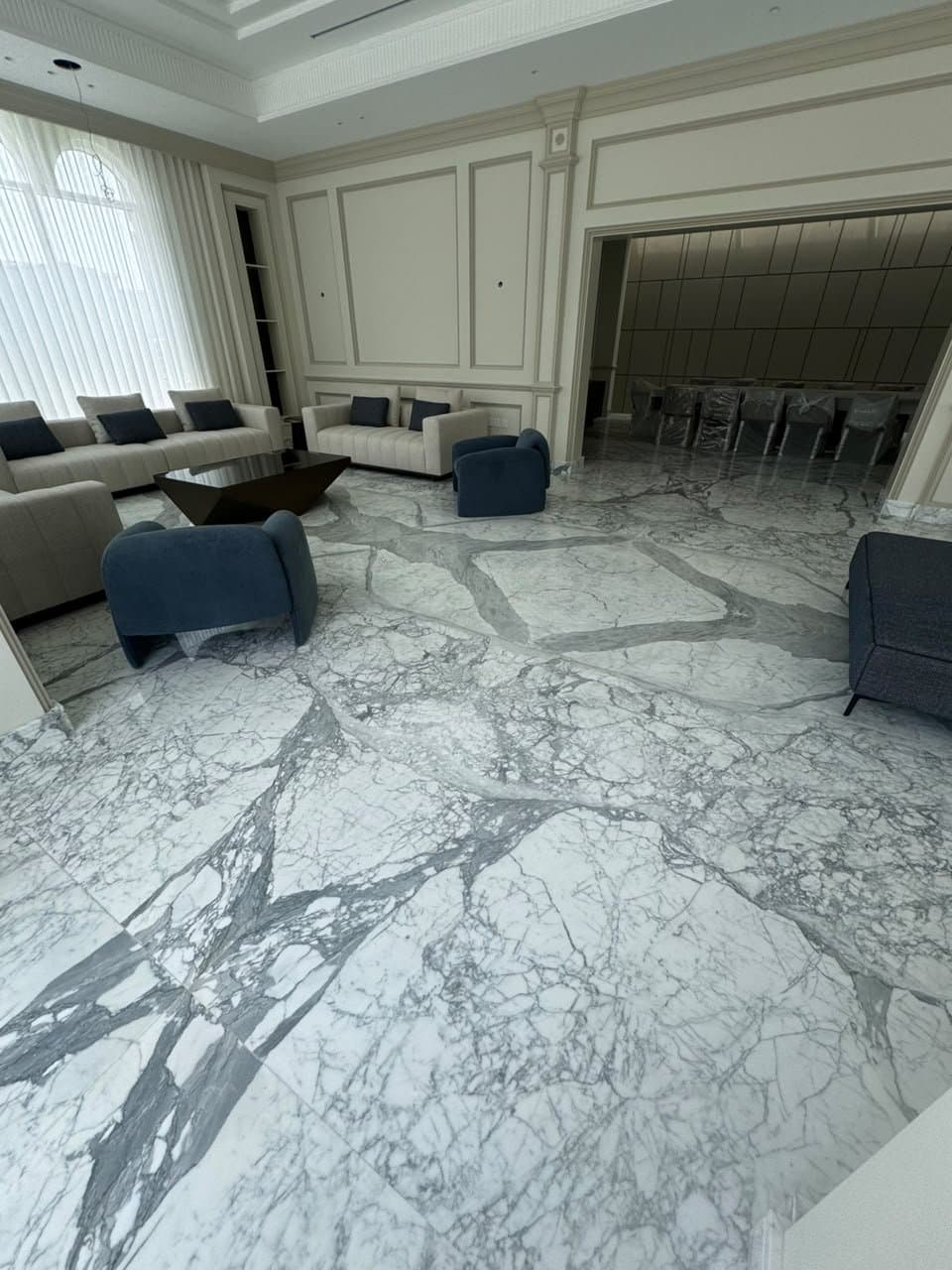 Bookmatched grey-veined marble flooring in a living room with navy armchairs