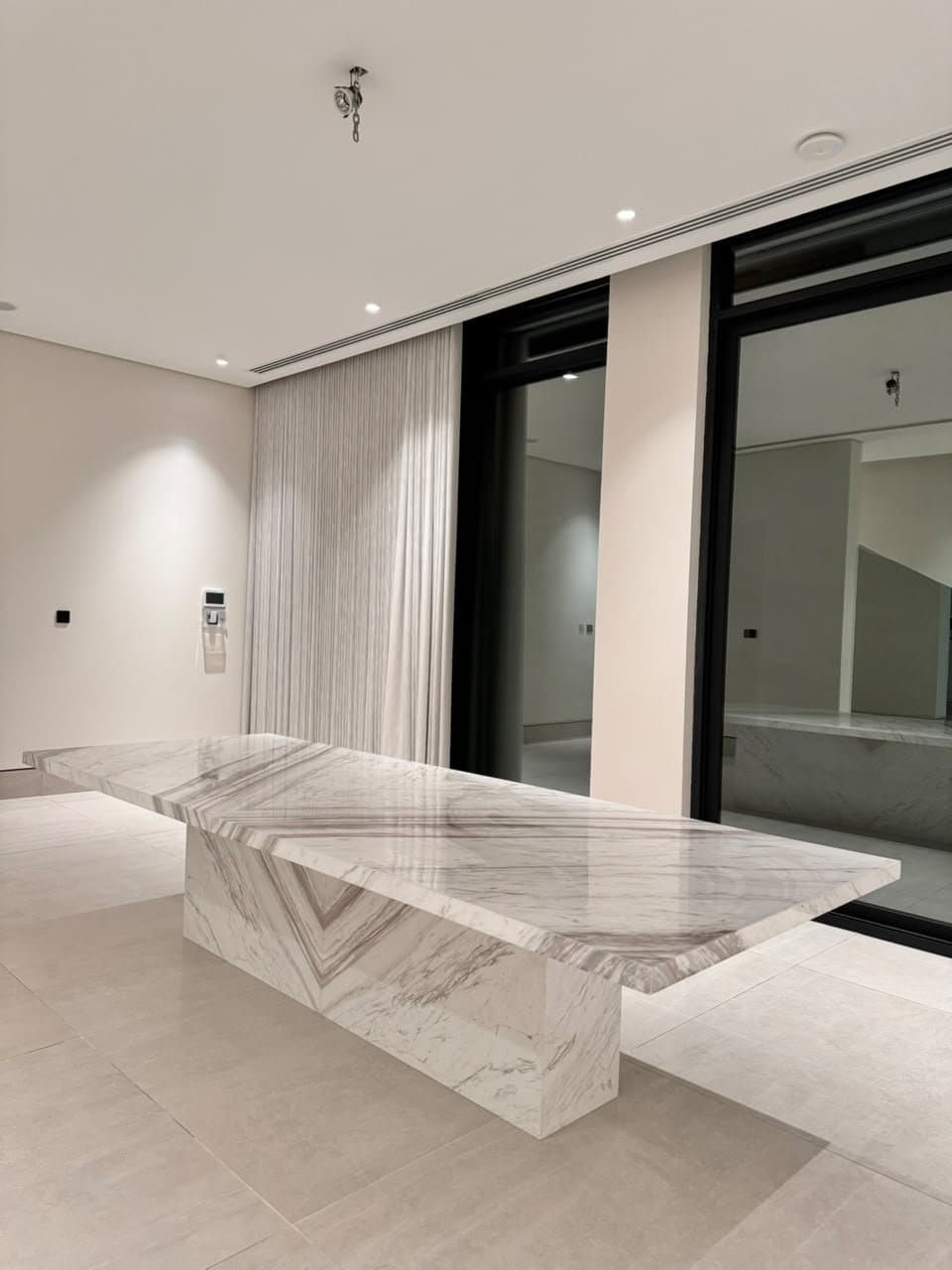 Long bookmatched marble dining table beneath a sheer curtain wall