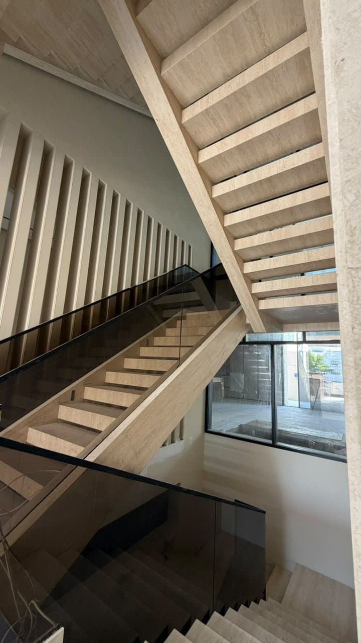 Travertine staircase with glass balustrade, seen from below against a fluted wall