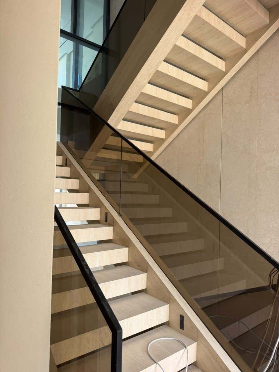 Travertine staircase with glass balustrade beside a fluted wall and floor-to-ceiling windows