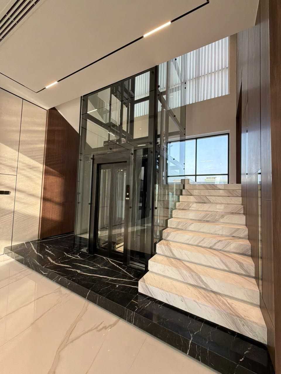 Travertine staircase with glass balustrade against fluted travertine wall paneling