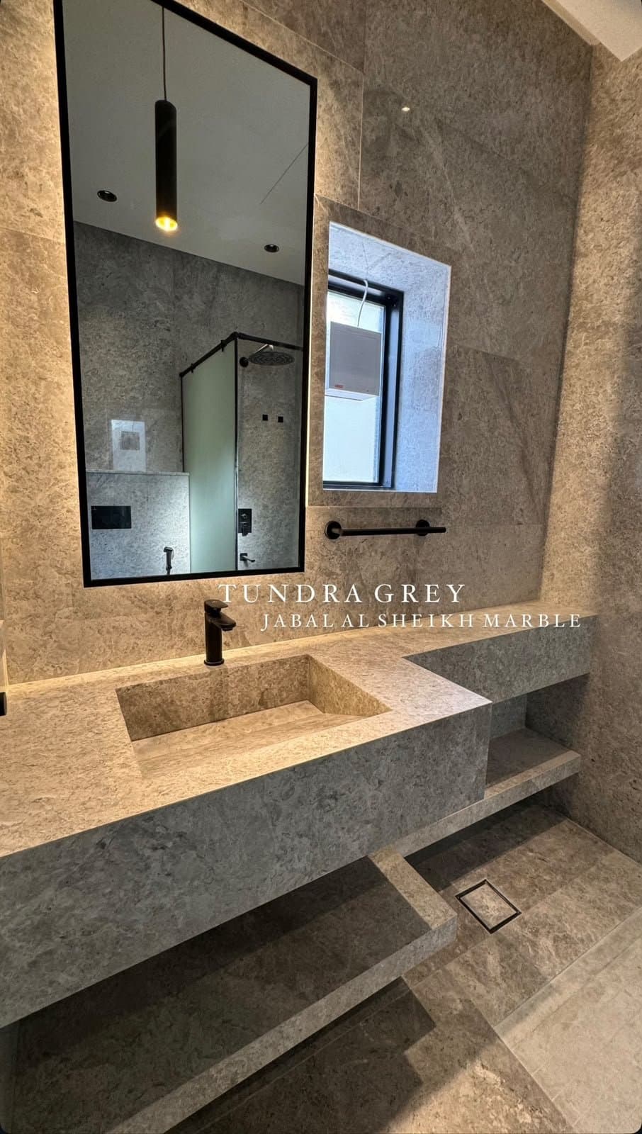 Tundra Grey marble vanity with carved sink and glass shower behind