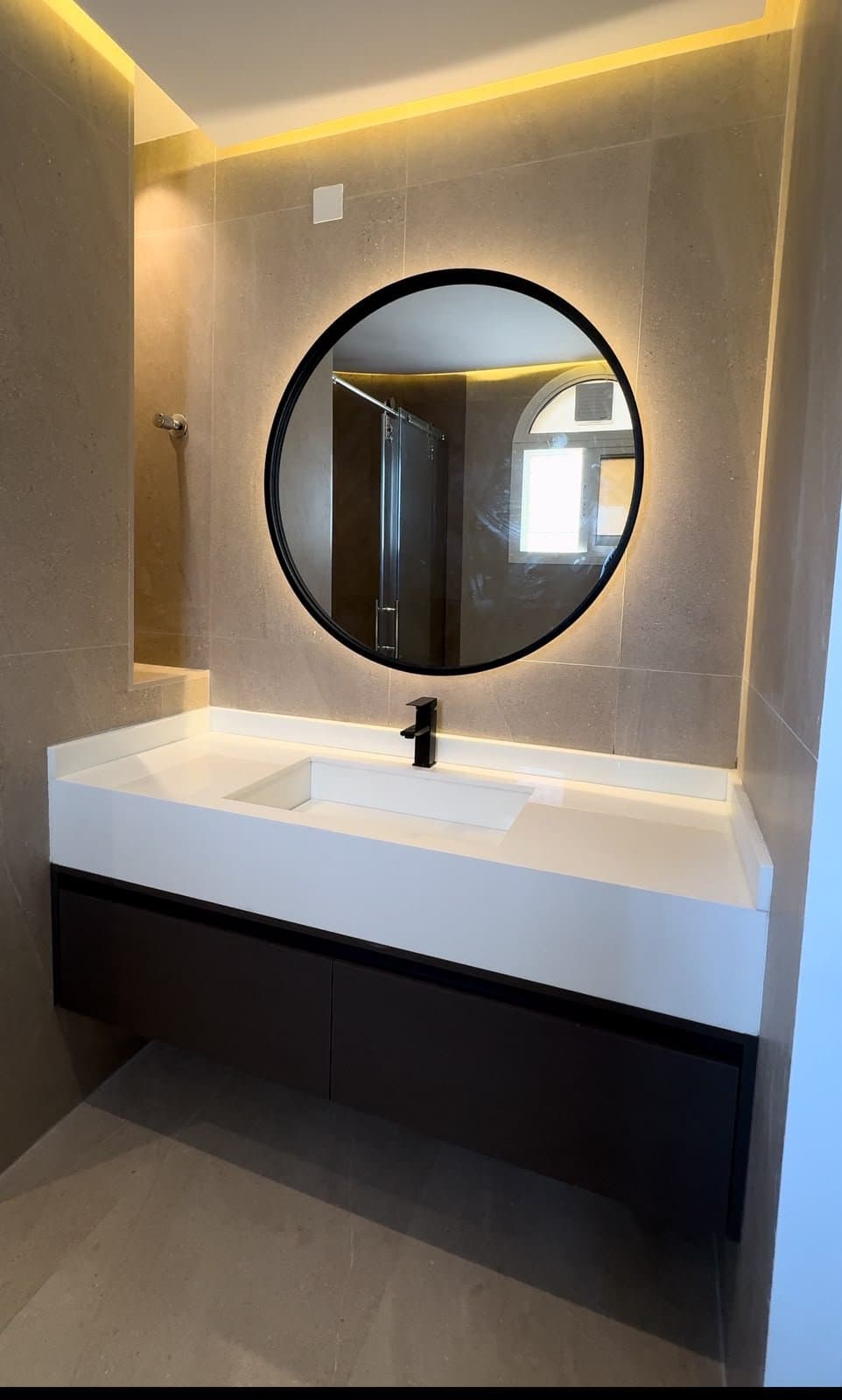 Beige stone vanity with round backlit mirror and black fixtures