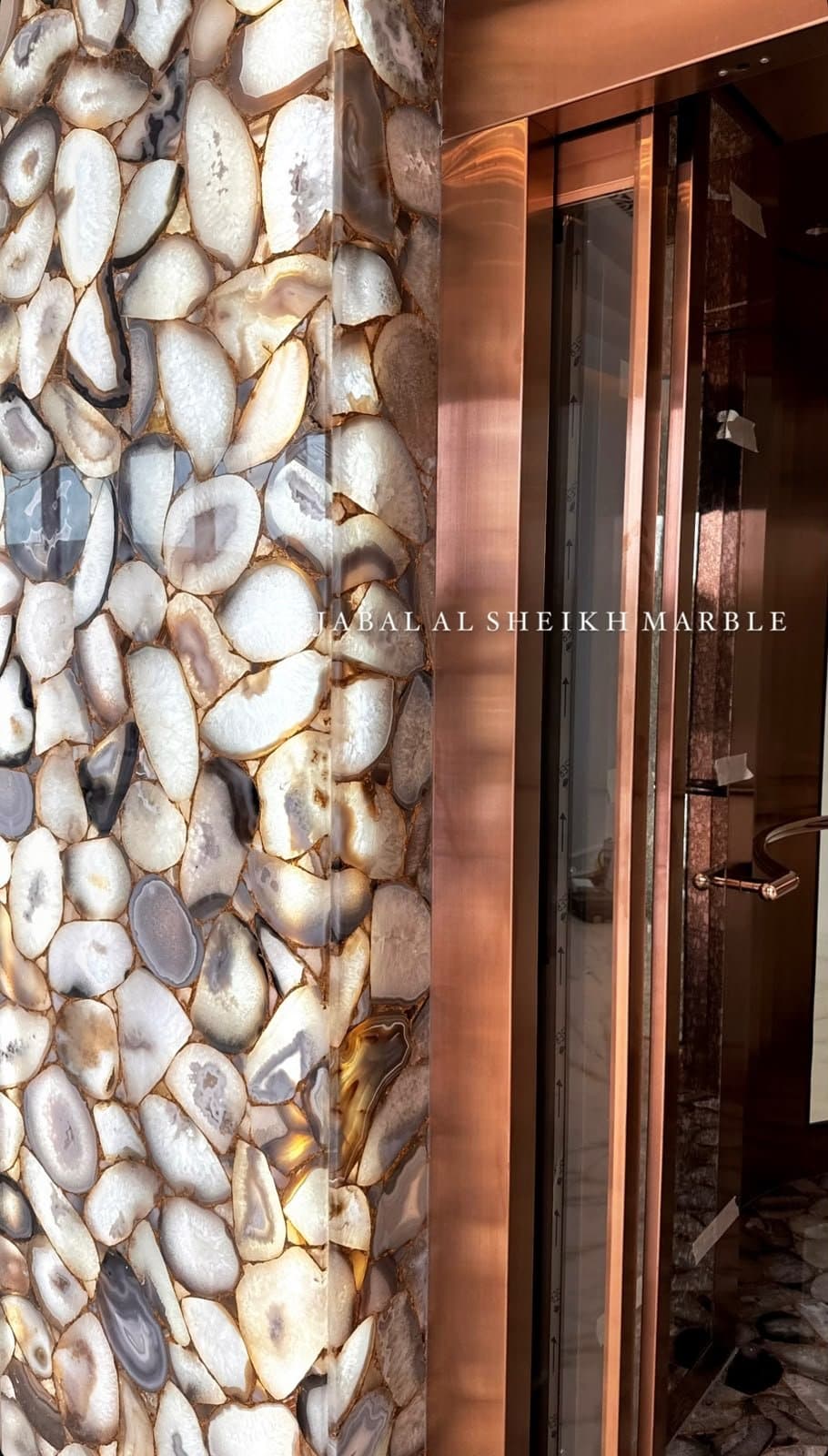 Backlit agate stone wall cladding beside a copper-framed elevator