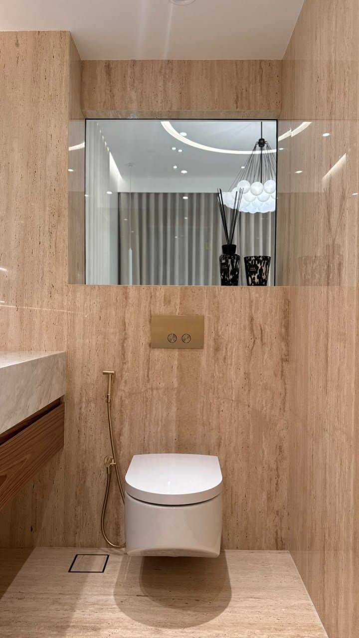 Travertine wall cladding in a powder room with mirror and gold fixtures
