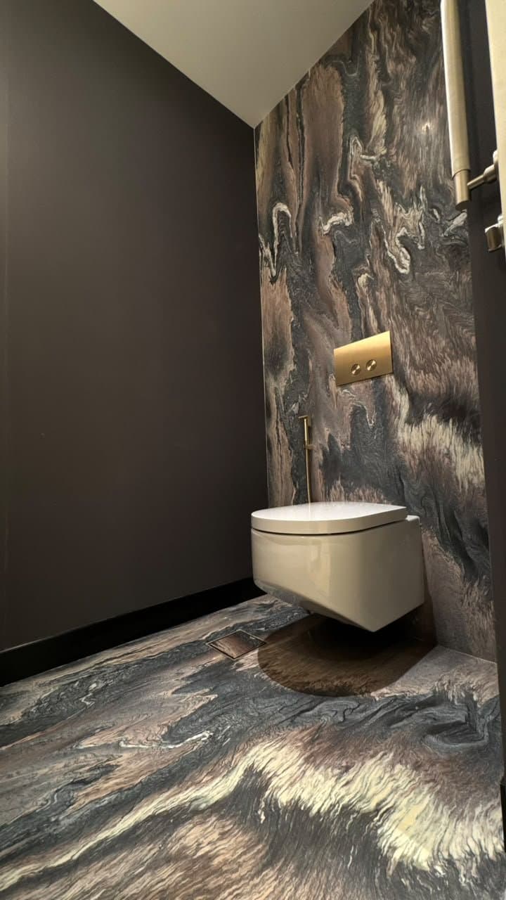 Dramatic swirled stone wall cladding in a powder room with brass fittings