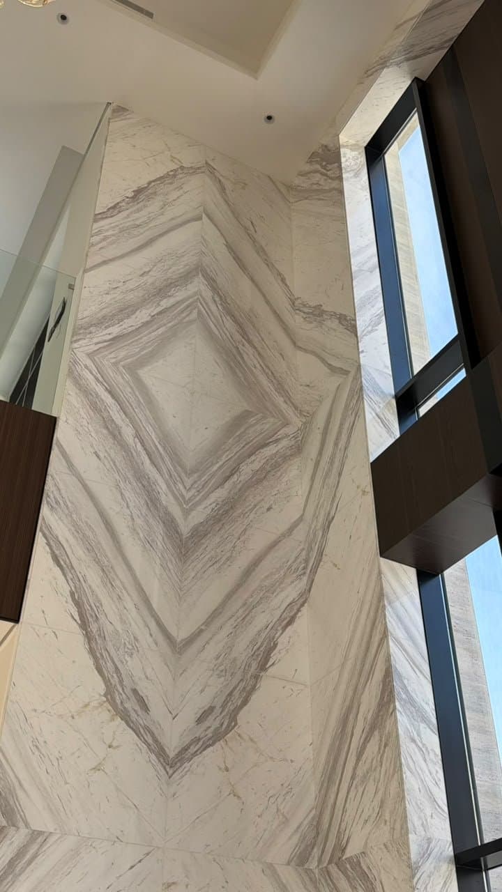 Bookmatched marble cladding rising two storeys beside floor-to-ceiling glazing