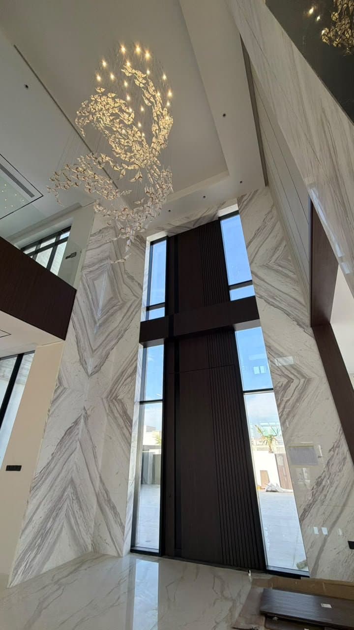 Bookmatched marble cladding in a double-height entrance hall with chandelier