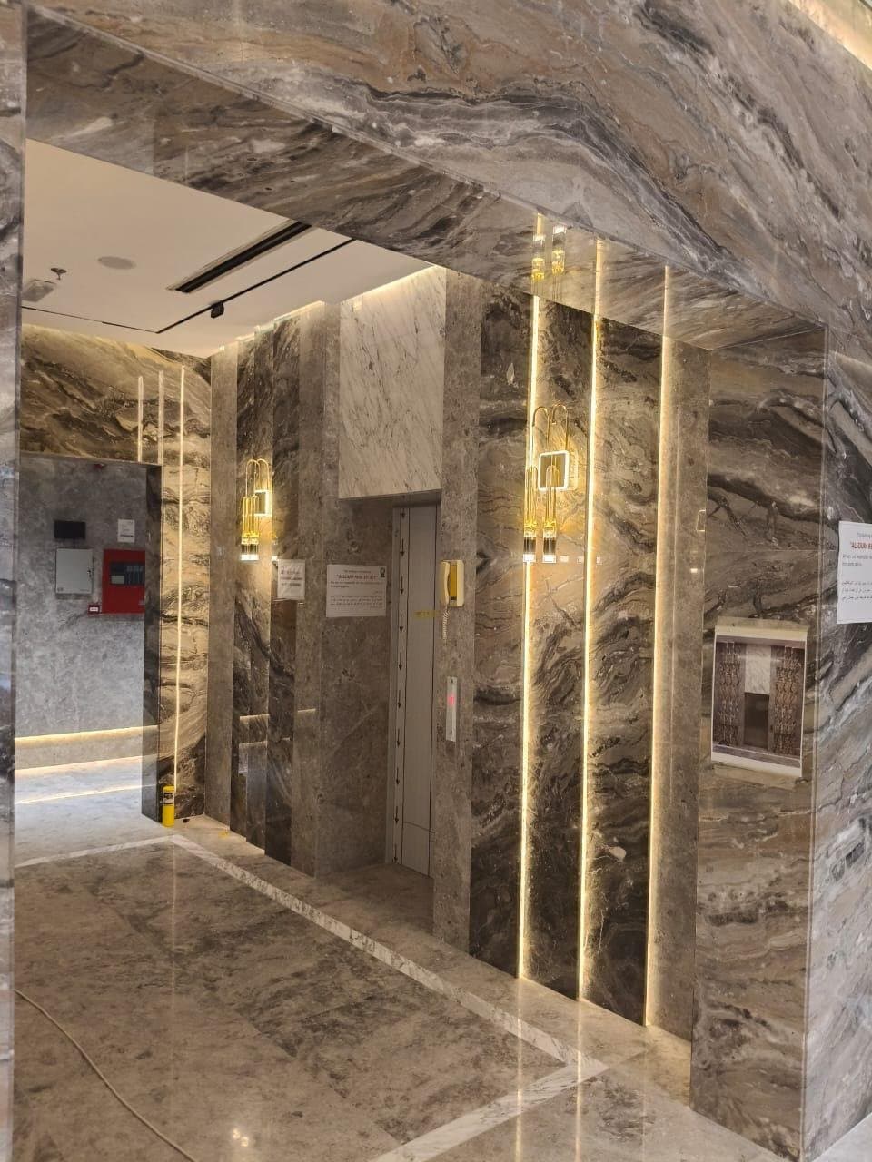Bookmatched stone wall cladding surrounding an elevator with brass accents