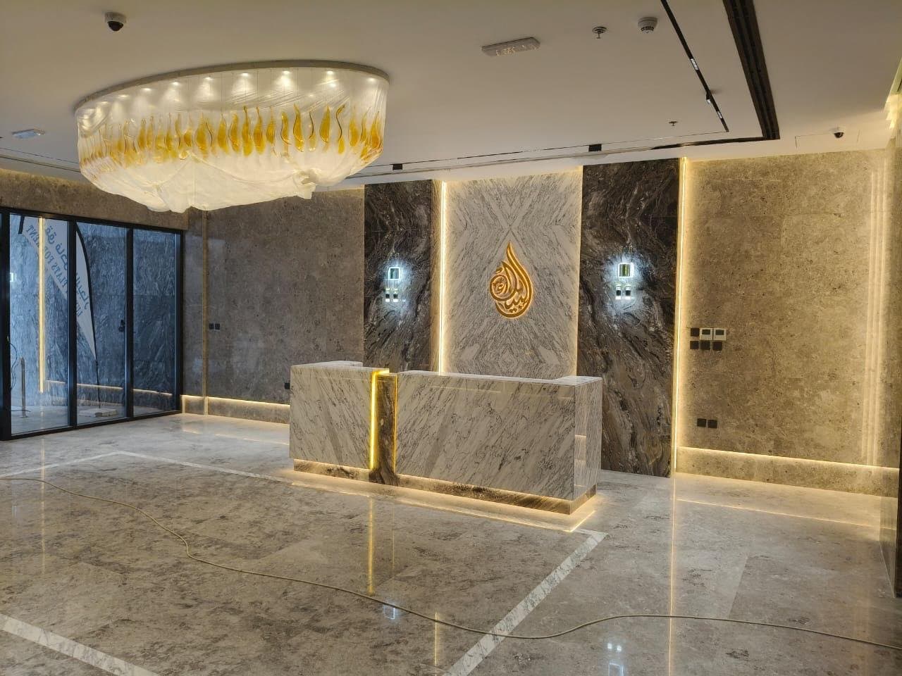 Bookmatched stone reception wall with backlit gold Arabic calligraphy