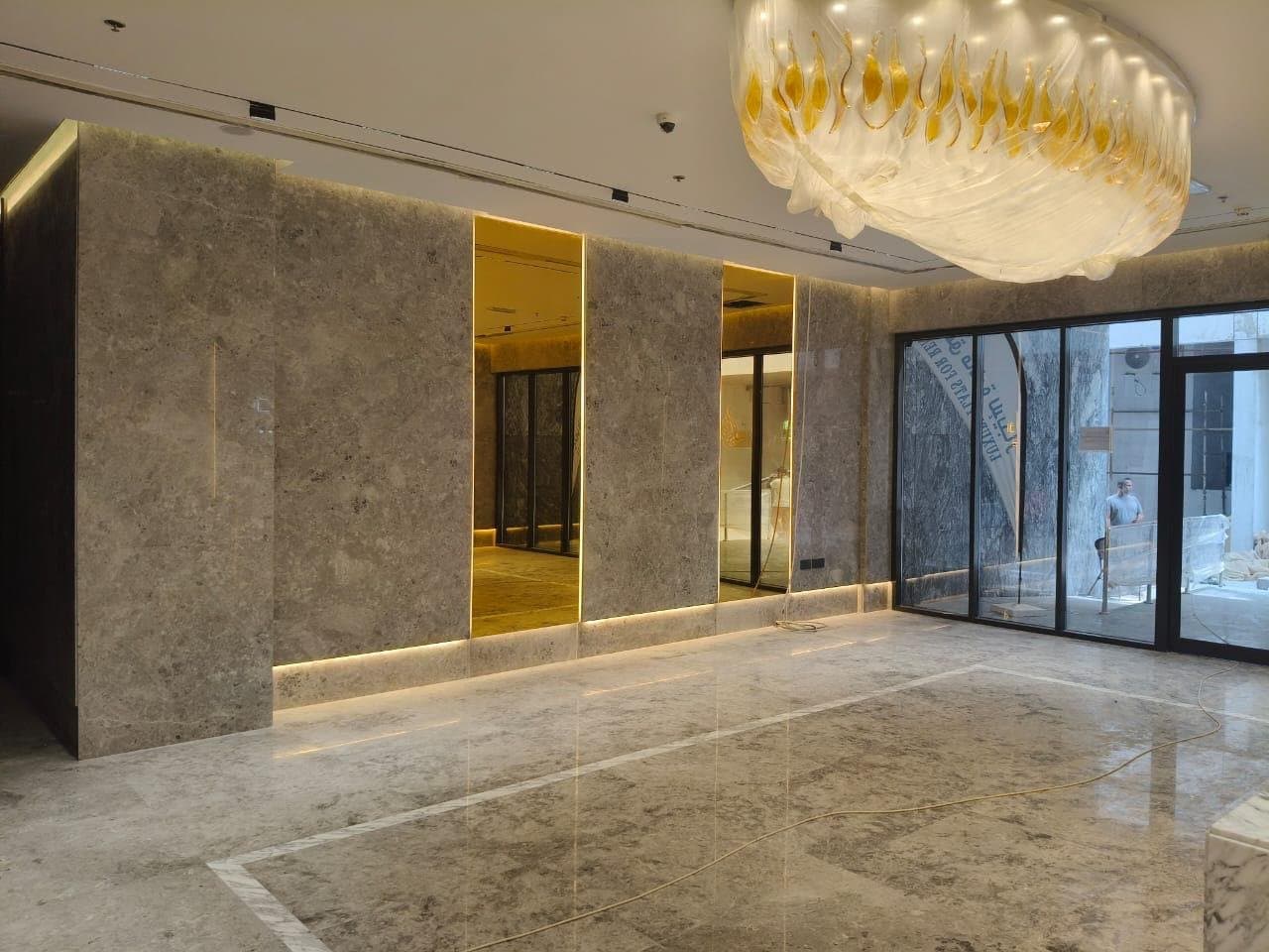 Bookmatched stone wall cladding in a reception area with backlit mirror insets
