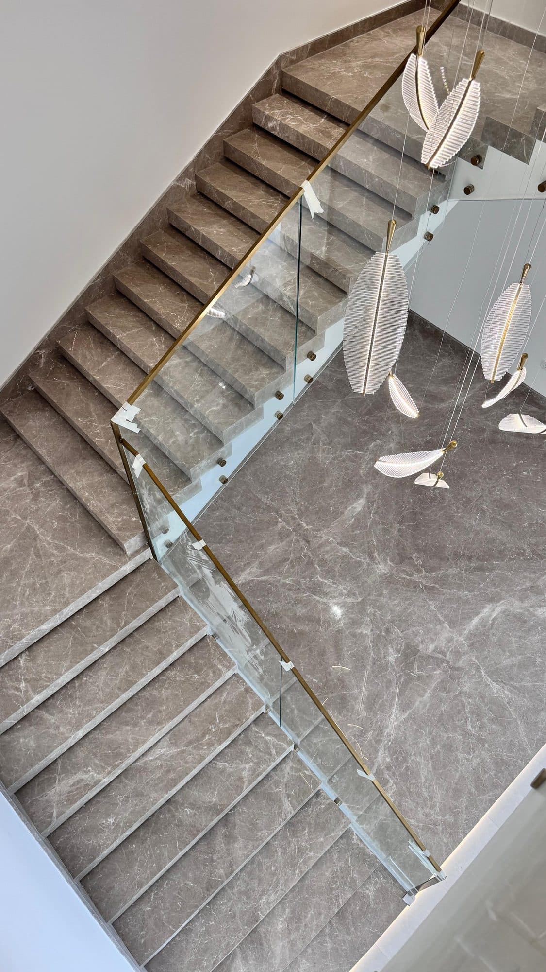 Grey marble staircase with glass balustrade and hanging feather lights