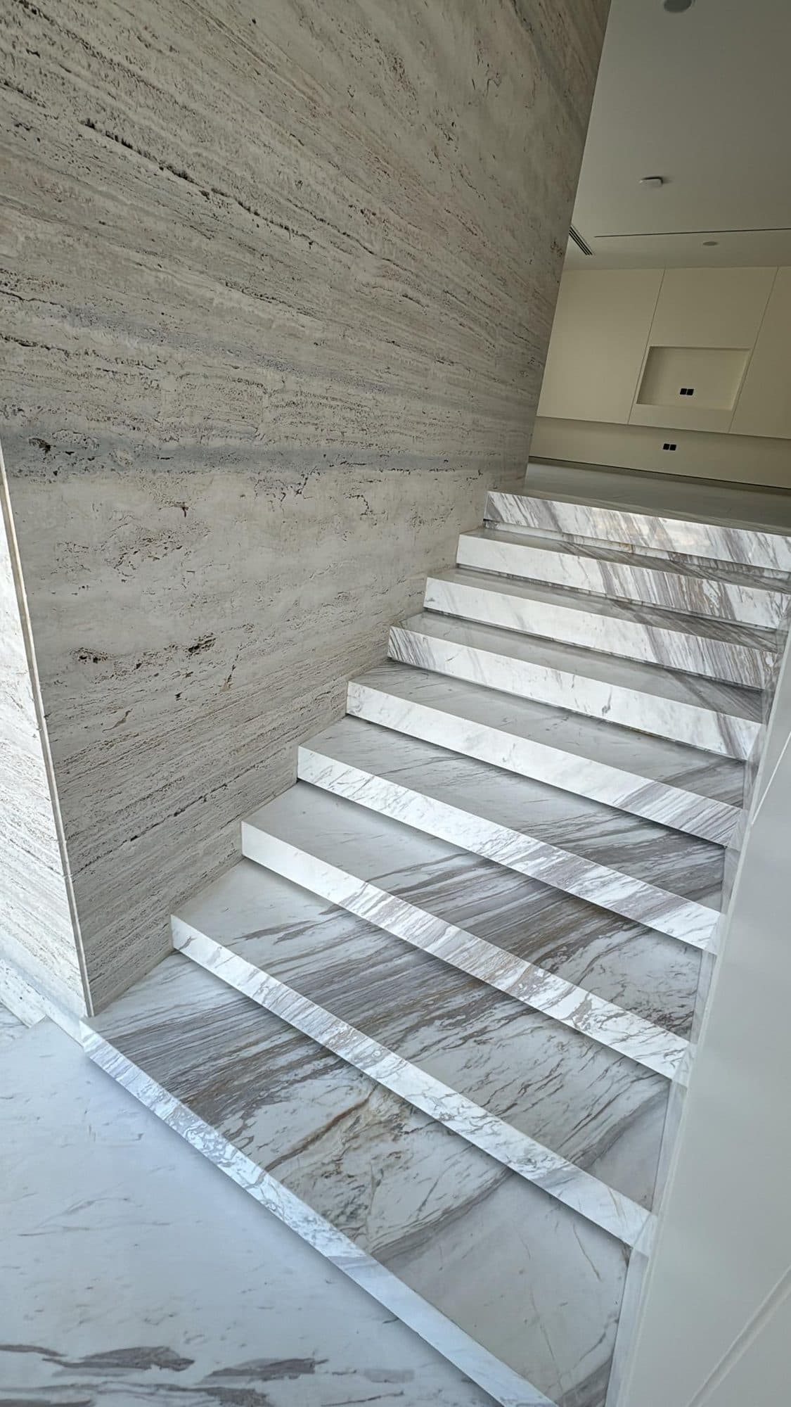 White marble staircase with book-matched veining against a travertine wall