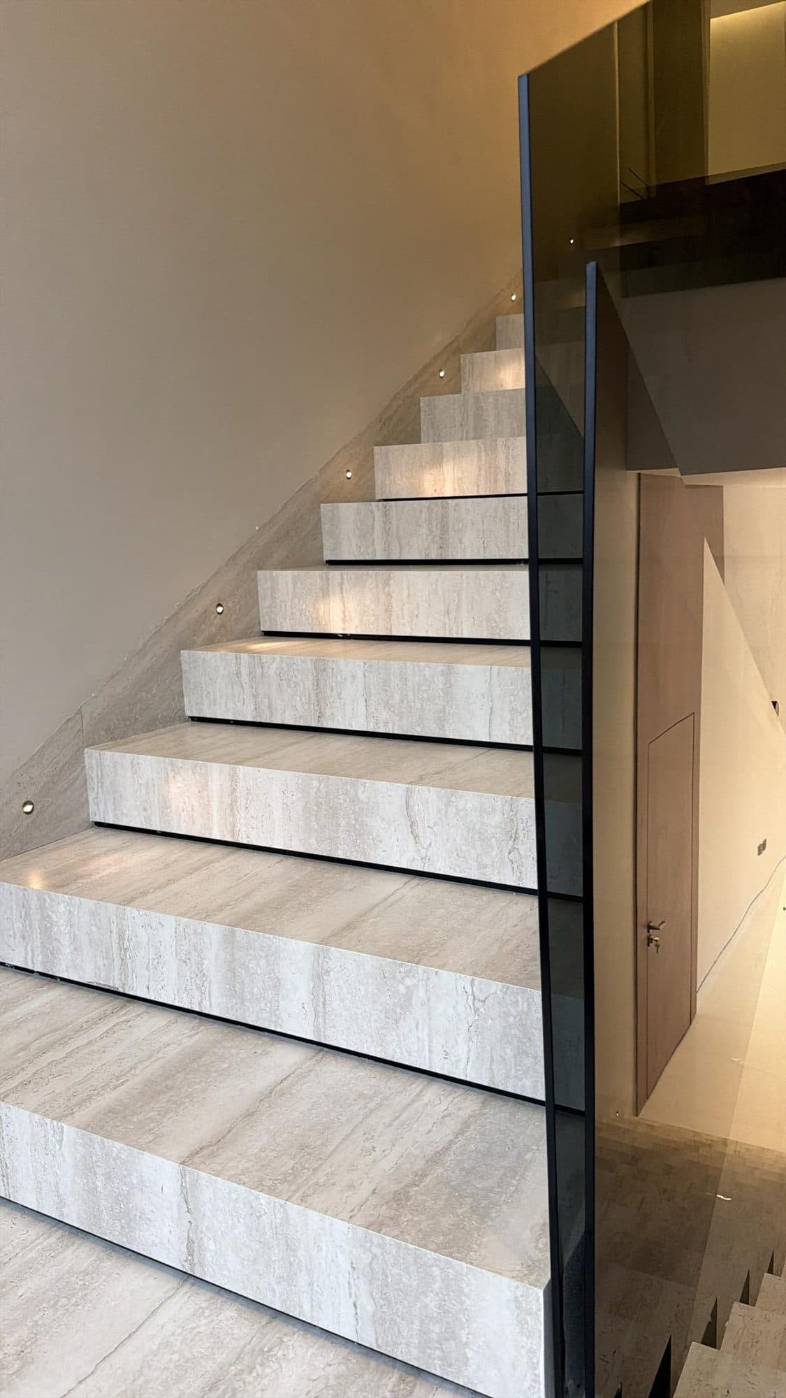 Travertine staircase with black metal trim and recessed lighting