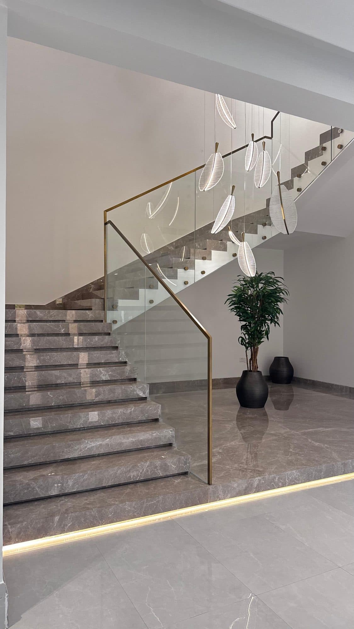 Grey marble staircase with brass handrail and hanging feather lights
