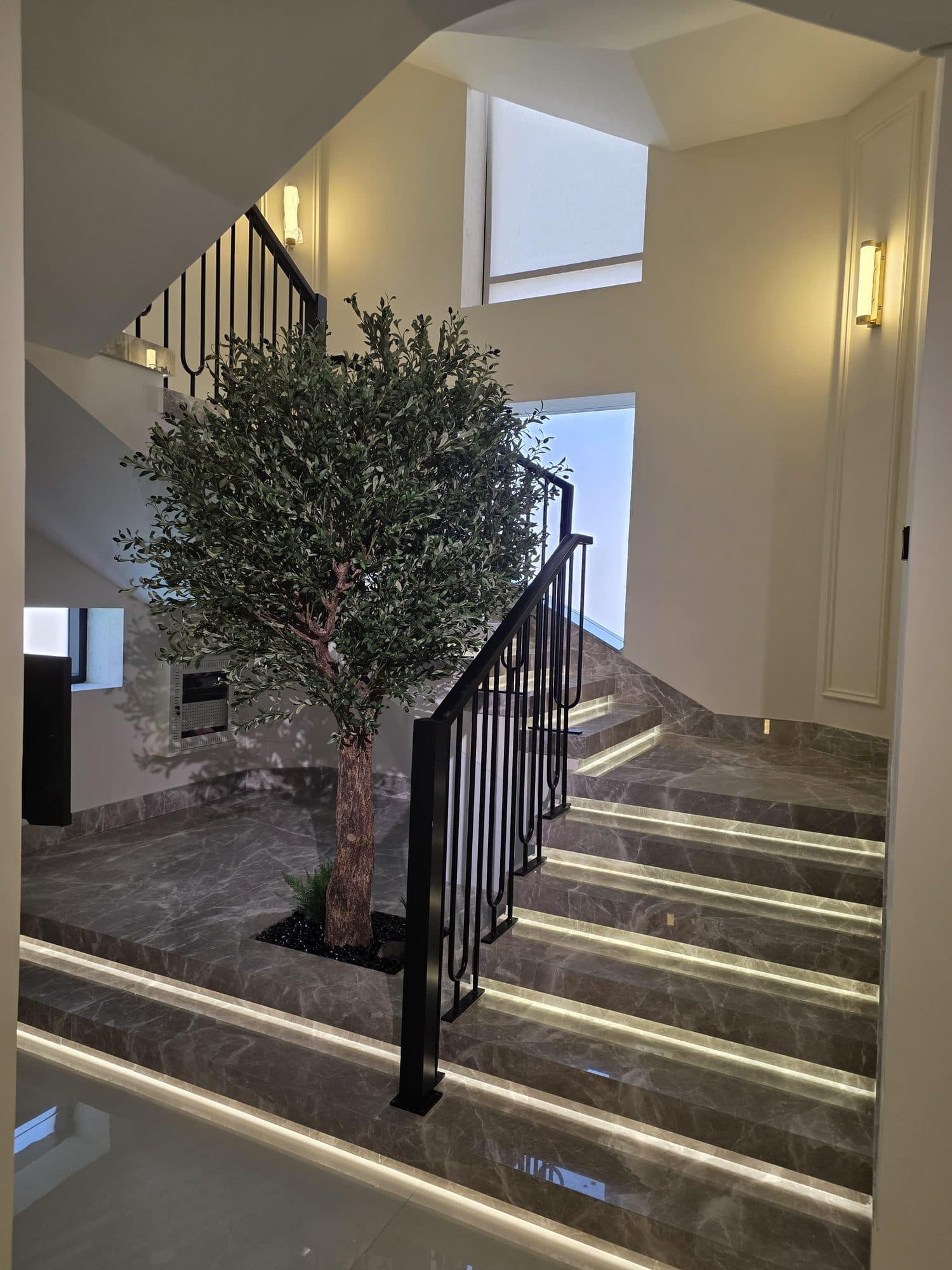 Grey marble staircase with black metal railing beside an olive tree